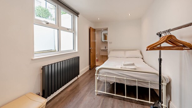 A bedroom with a bed, a radiator, a wooden hanger rack, and a window. - Host Stay Clarendon Violet (Brighton)
