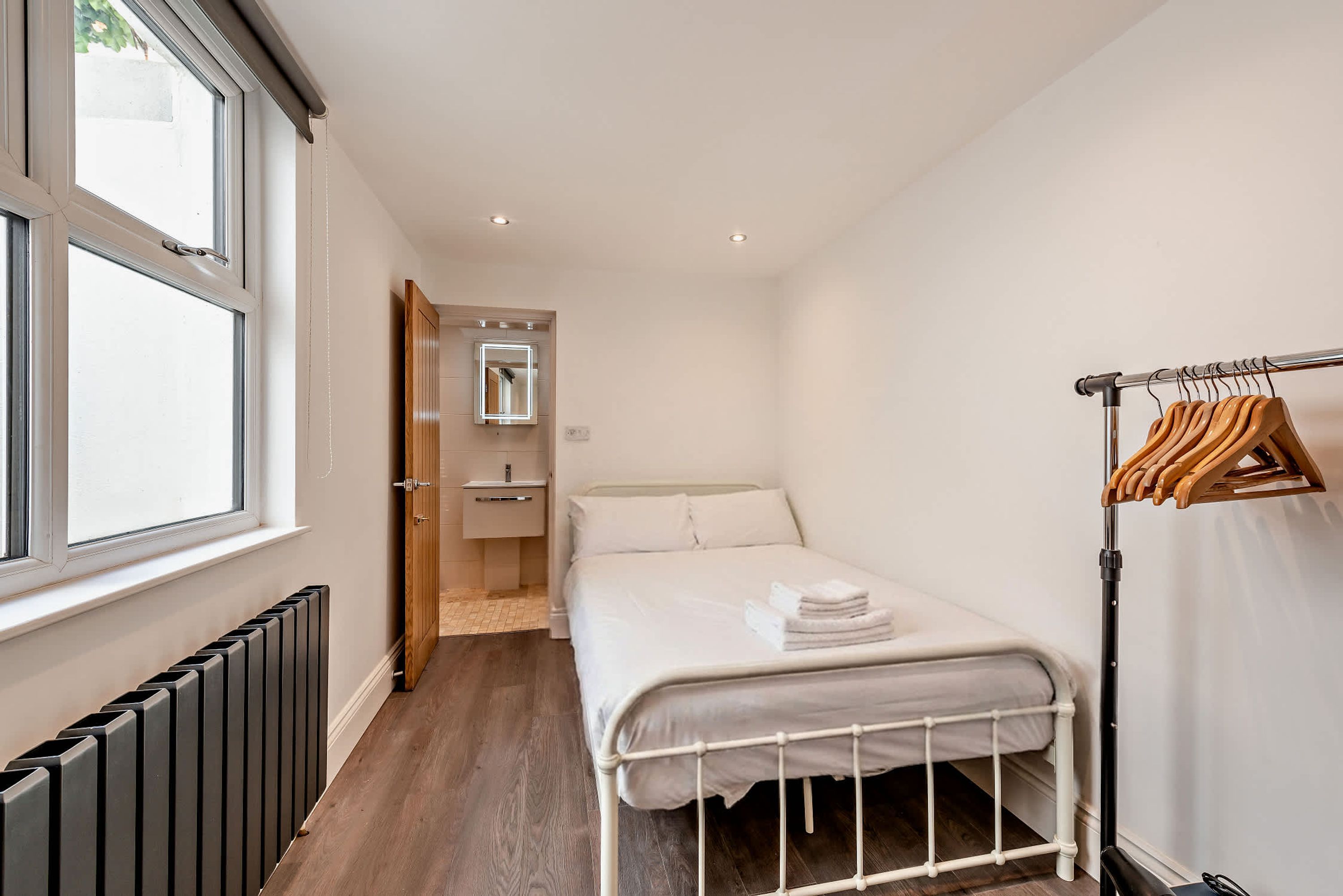 Un dormitorio pequeño y ordenado con una cama individual, un radiador, una puerta de madera que da al baño y un perchero.