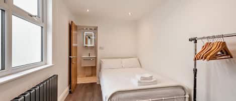 A small, neatly organized bedroom with a single bed, a radiator, a wooden door leading to a bathroom, and a clothing rack.