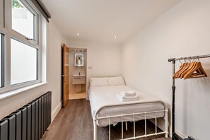 A small, neatly organized bedroom with a single bed, a radiator, a wooden door leading to a bathroom, and a clothing rack. - Host Stay Clarendon Violet (Brighton)