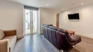 A modern living room with a sofa, a reclining chair, a television mounted on the wall, and a sliding glass door leading to an outdoor area. - Host Stay Clarendon Violet (Brighton)