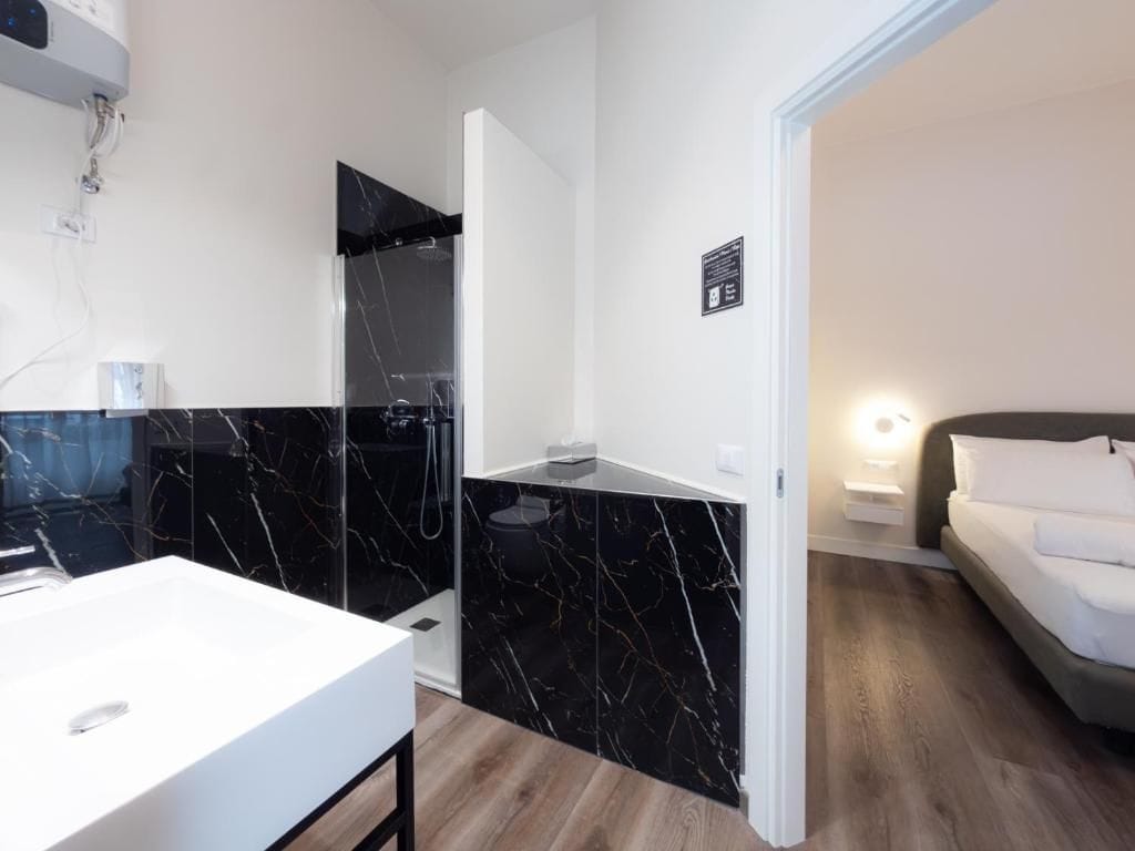 Ein modernes Badezimmer mit einem weißen Waschbecken, einer schwarzen Duschkabine aus Marmor und einer weißen Toilette.