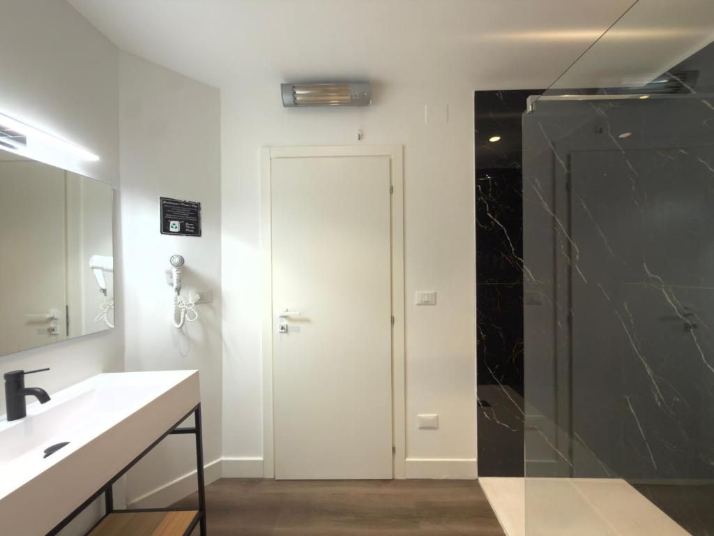 Une salle de bain moderne avec un meuble-lavabo blanc, un grand miroir, une porte et une cabine de douche en marbre.