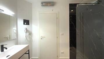Une salle de bain moderne avec un meuble-lavabo blanc, un grand miroir, une porte et une cabine de douche en marbre.