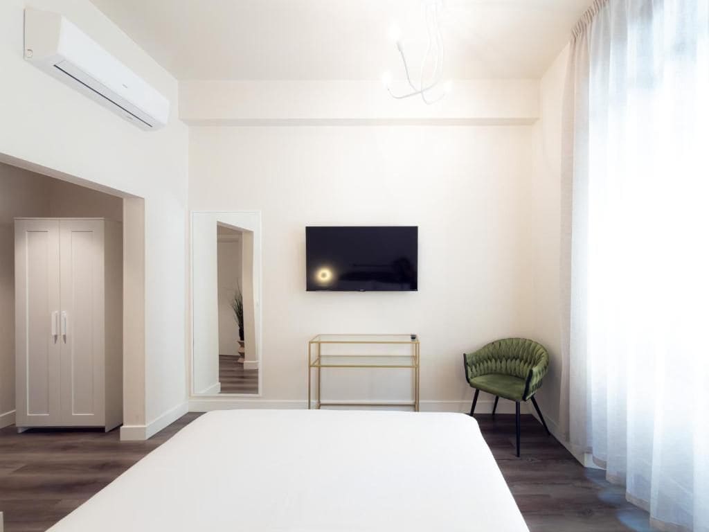 A bedroom with a bed, a television mounted on the wall, a green chair, and a white wardrobe.