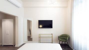 A bedroom with a bed, a television mounted on the wall, a green chair, and a white wardrobe.