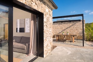 A modern stone building with a glass door leading to a living area with a sofa and a table with chairs. - Villa Iron Lady Labin Private Pool & Sea View (Labin)