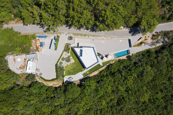An aerial view of a property with a swimming pool, a parking lot, and a building with a flat roof. - Villa Awesome Lodge (Rasa)