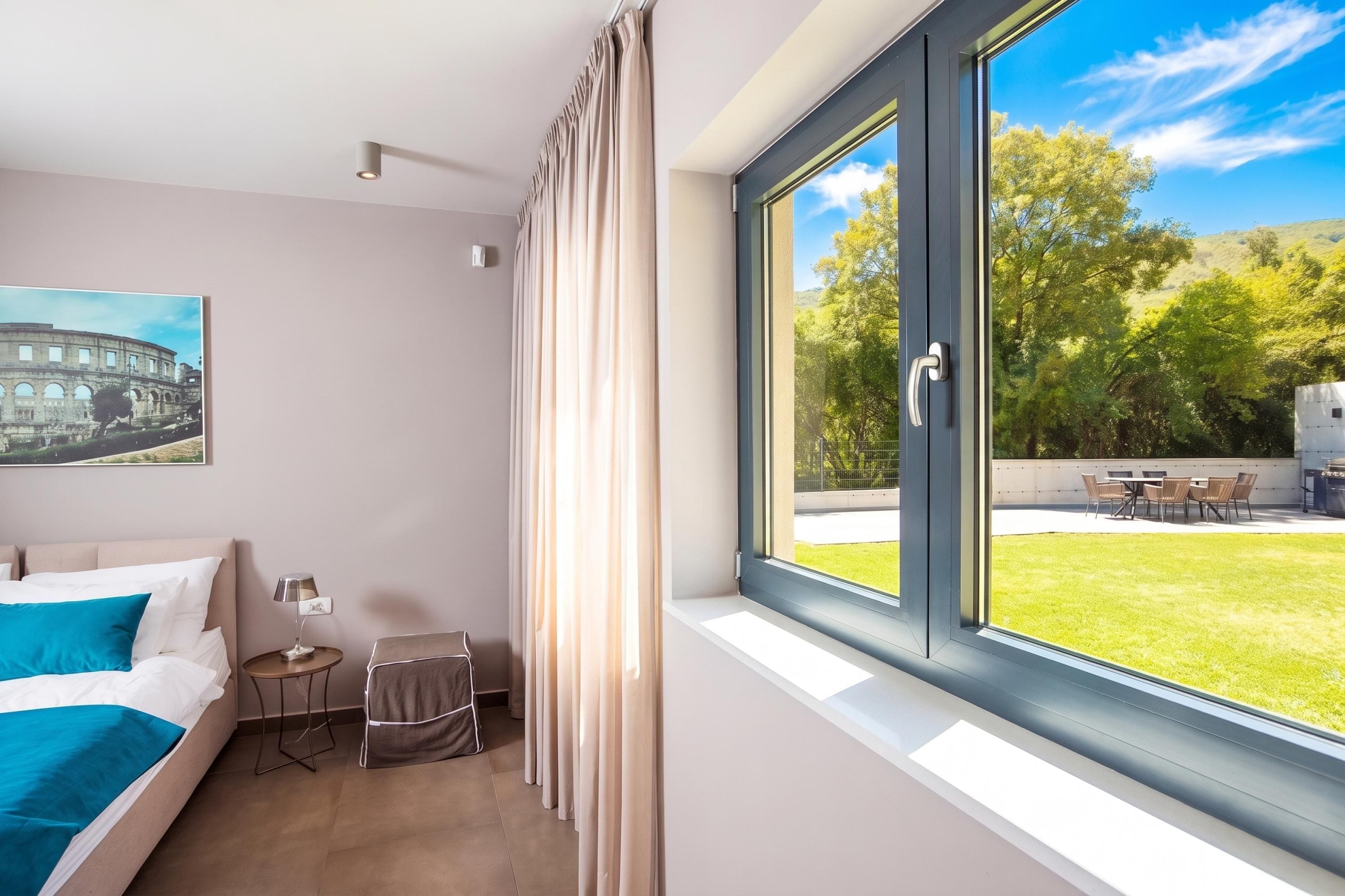 Une chambre d’hôtel avec un lit, une petite table avec une lampe, une chaise, une fenêtre avec des rideaux et une vue sur un espace verdoyant.