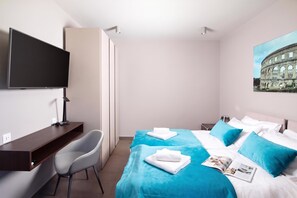 Habitación de hotel con cama, escritorio, silla, televisor y un cuadro de un edificio histórico.