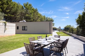 Un área de comedor al aire libre con una mesa dispuesta para cuatro, rodeada de sillas, y un edificio moderno al fondo.