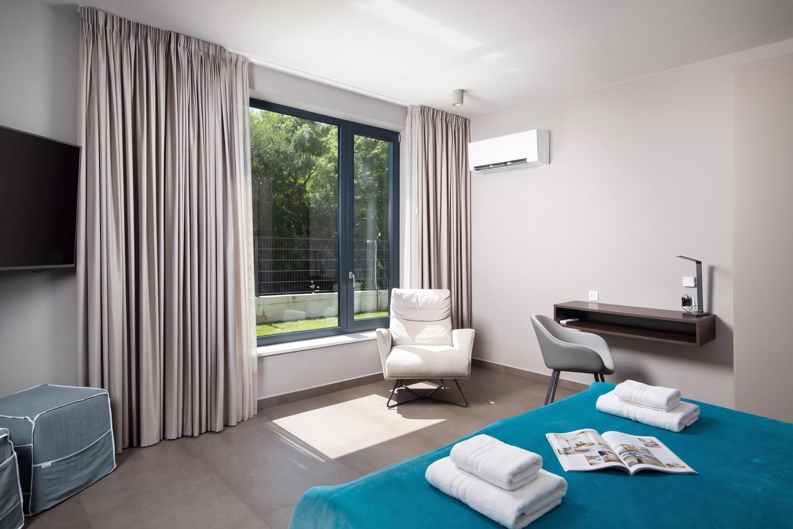 A hotel room with a bed, a desk, a chair, a TV, and a window with curtains.
