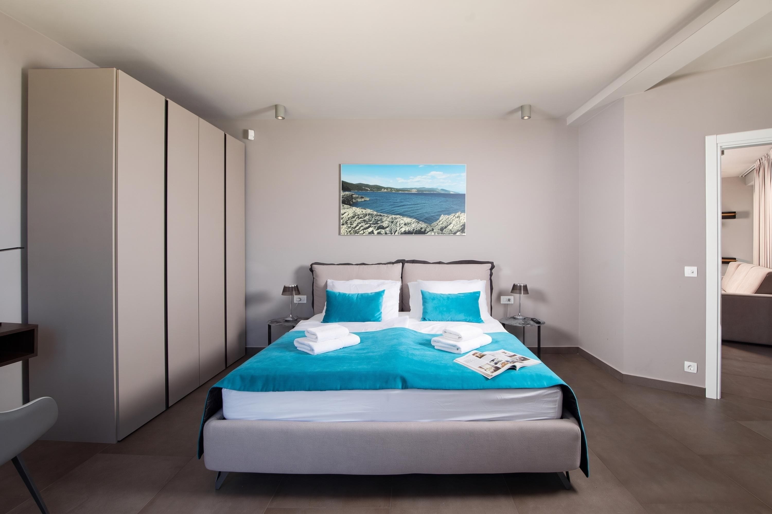 Un dormitorio moderno con una cama grande, dos mesitas de noche, un armario y vistas al mar.