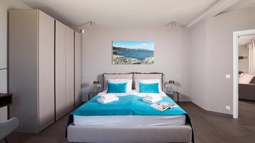 Un dormitorio moderno con una cama grande, dos mesitas de noche, un armario y vistas al mar.