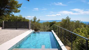 Una piscina rectangular con agua azul cristalina, rodeada por una solana de baldosas blancas y una barandilla de metal negro.