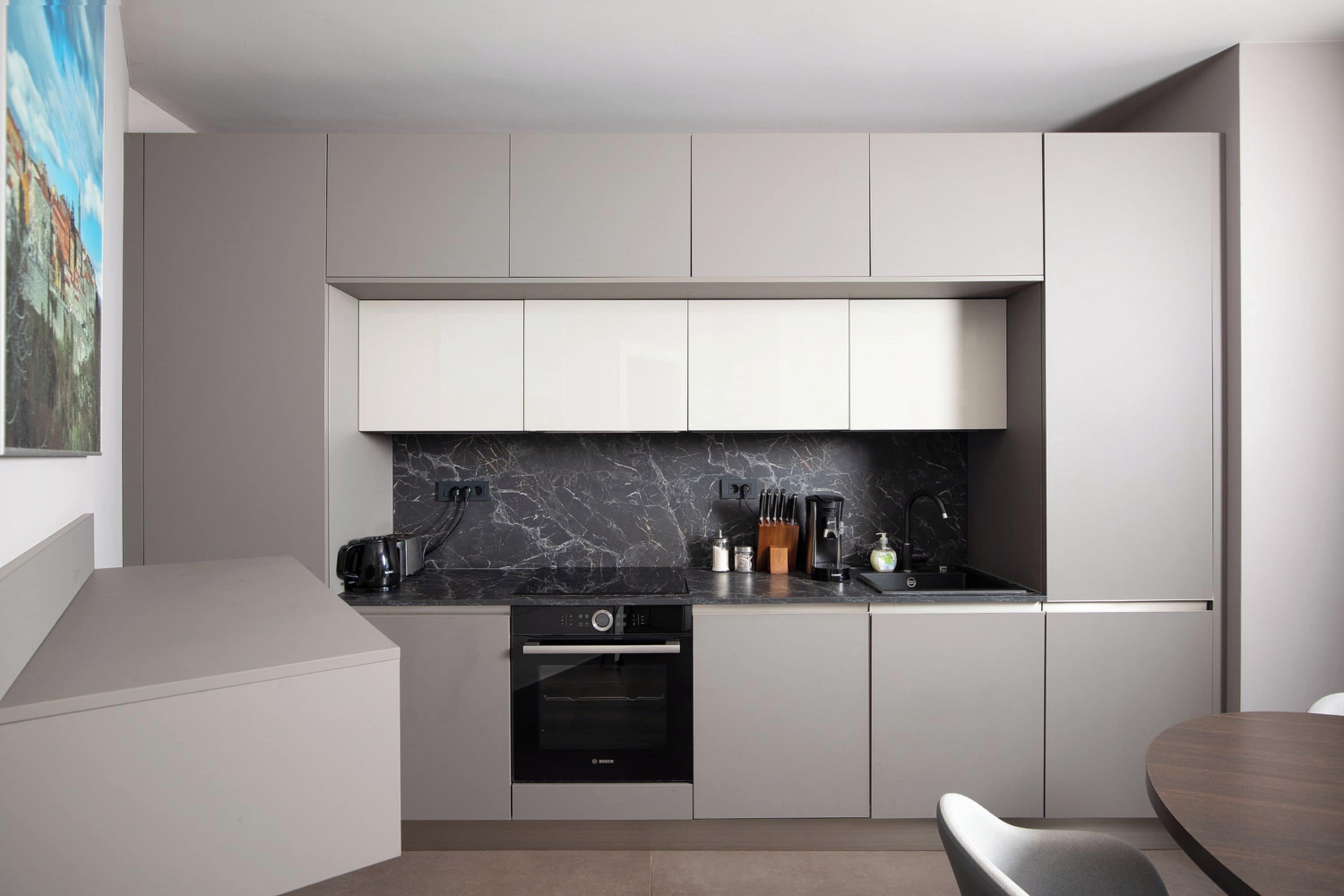 Una cocina moderna con armarios blancos, horno Bosch y salpicadero de mármol.