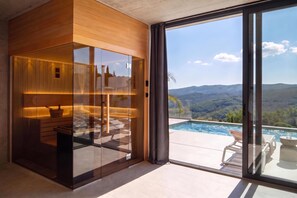 Ein modernes Interieur mit einer Glasabtrennung, einer Wand aus Holzpaneelen und Blick auf eine Berglandschaft.