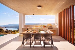 A modern kitchen with a large island, dining area with chairs, and a view of the sea. - Villa Immortella Luxury Pool & Spa Retreat (Labin)