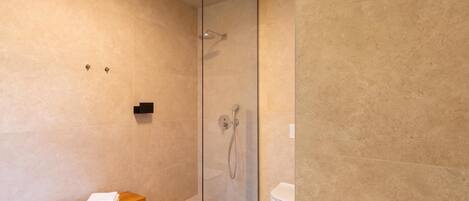 A modern bathroom with a glass shower enclosure, a wooden bench with towels, and a toilet.