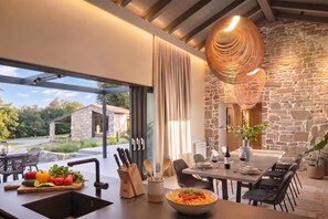 Una cocina moderna con pared de piedra, zona de comedor con mesa para dos y vistas al exterior.