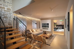 A modern living room with a staircase, a sofa, a coffee table, and a TV. - Villa Baracchi 4 BDR Pool Villa With Sauna in Krsan (Krsan)