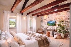 A bedroom with a stone wall, a bed with white linens, a wooden ceiling, and a window with curtains. - Villa Baracchi 4 BDR Pool Villa With Sauna in Krsan (Krsan)
