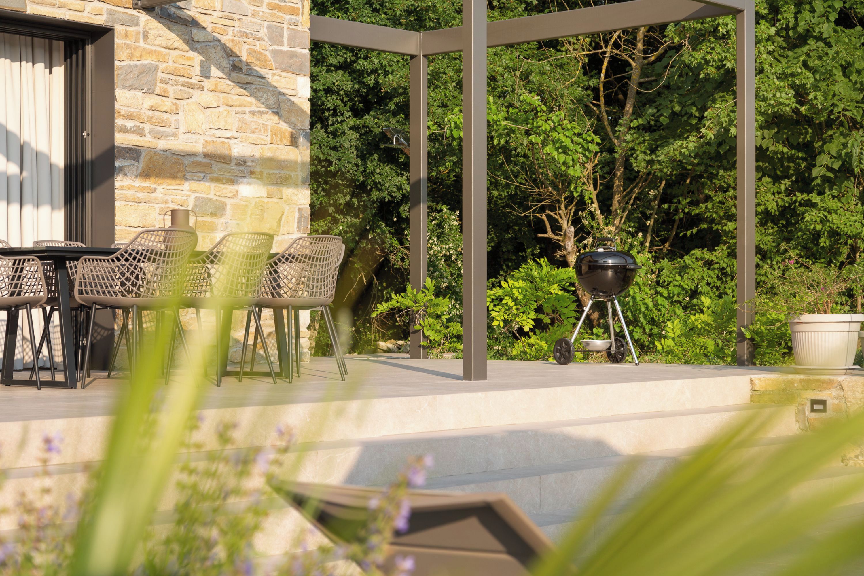 An outdoor patio with a stone wall, a grill, and outdoor furniture.