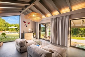 A modern interior with a sofa, a dining area, and a view of a garden. - Villa Baracchi 4 BDR Pool Villa With Sauna in Krsan (Krsan)