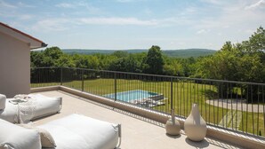 Ein Balkon mit Pool, weißen Gartenmöbeln und Blick auf eine grüne Landschaft.