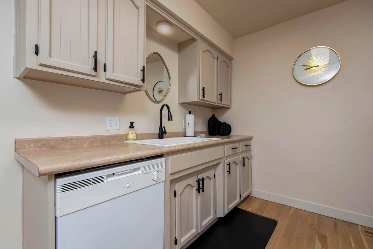 Una cocina moderna con armarios blancos, lavavajillas integrado, un lavabo y un reloj montado en la pared.