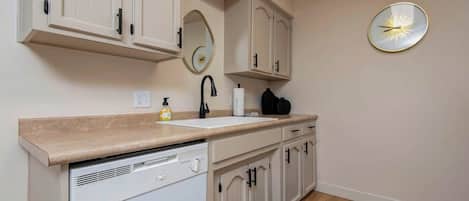 Una cocina moderna con armarios blancos, lavavajillas integrado, un lavabo y un reloj montado en la pared.