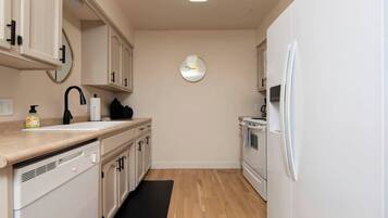 Una cocina compacta con armarios blancos, un grifo negro, un reloj en la pared y un refrigerador blanco.