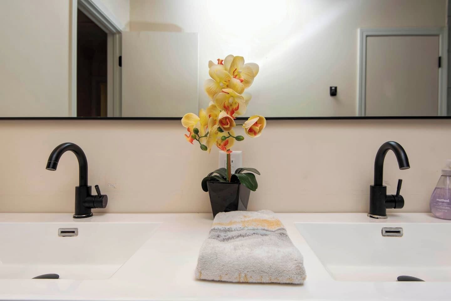 A bathroom with two sinks, a towel, and a potted orchid.