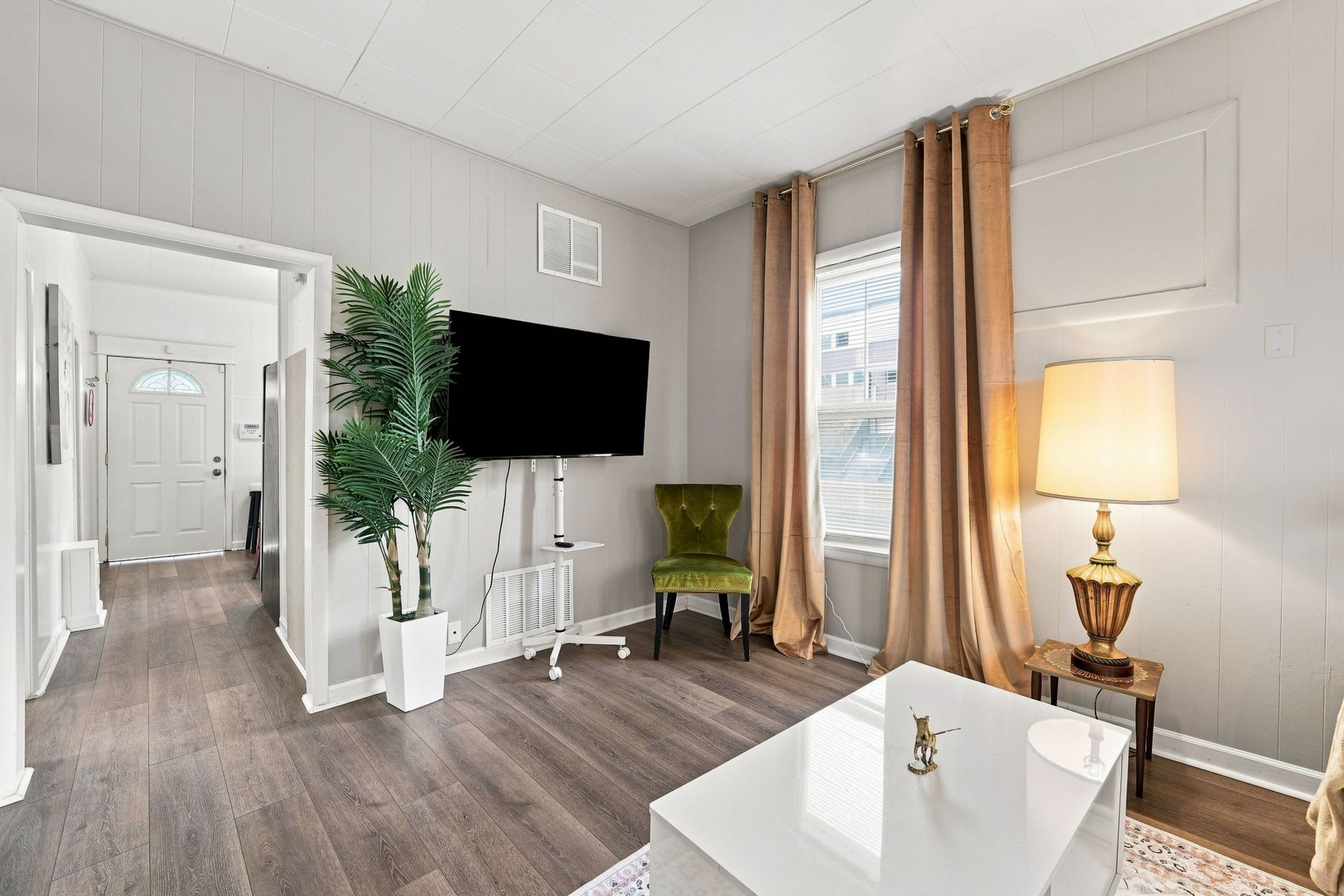 Una sala de estar moderna con un televisor de pantalla plana, un sillón verde, una mesa de centro blanca y una lámpara.