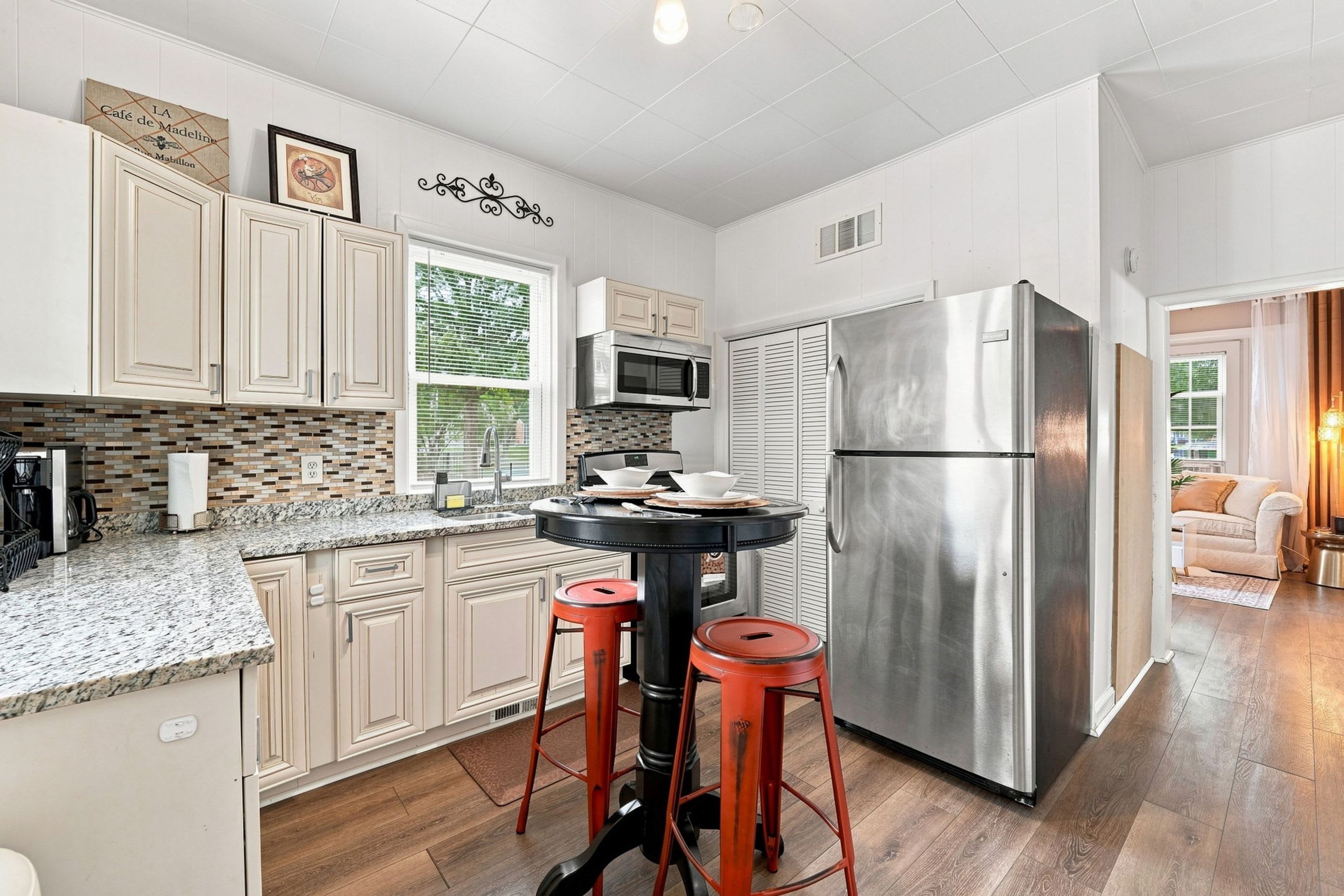 A modern kitchen with a stainless steel refrigerator, a microwave, and a dining area with stools.