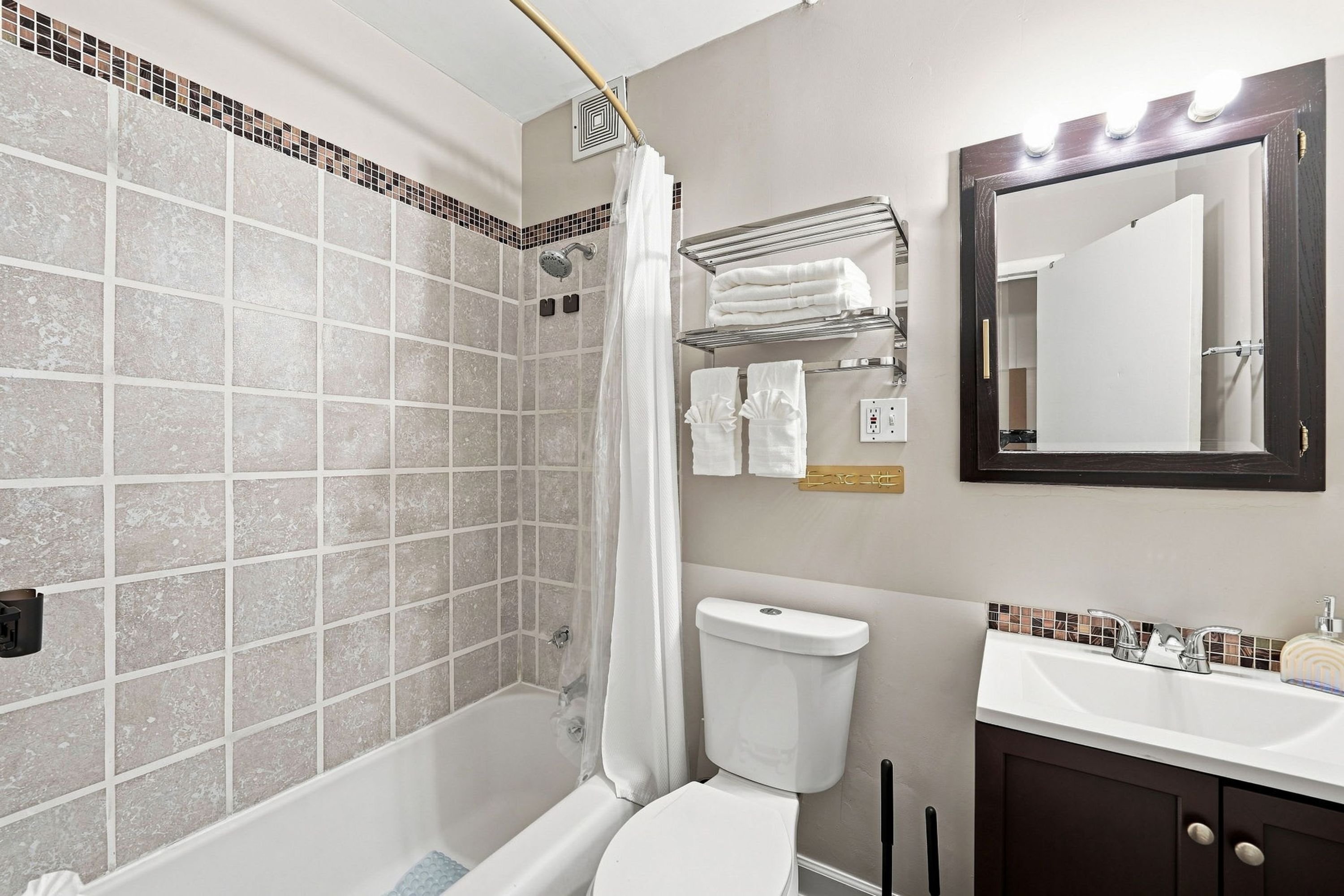 A bathroom with a shower, toilet, sink, and a mirror.