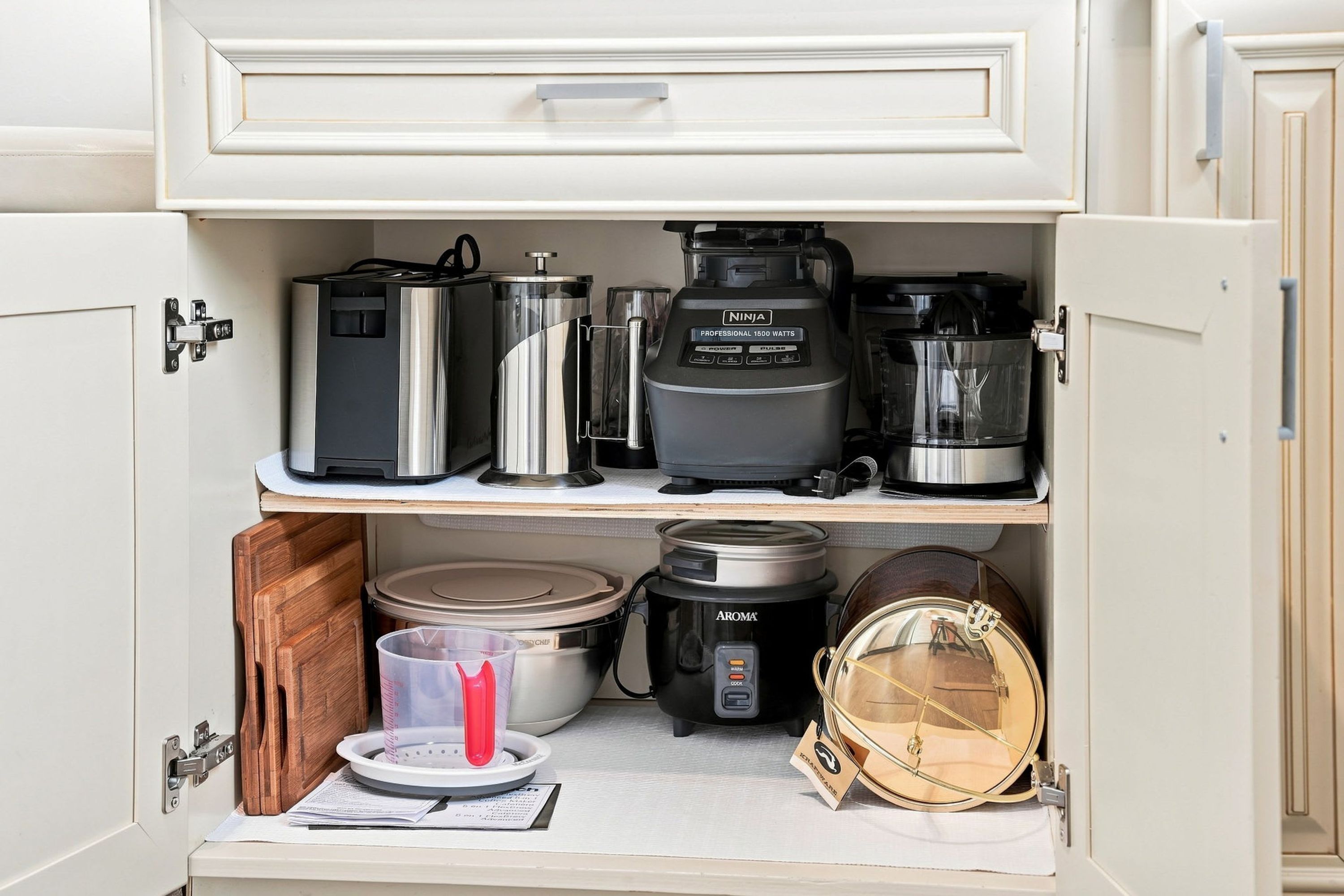 Un mueble de cocina con varios electrodomésticos, incluyendo una cafetera, una cocedora de arroz y una olla de cocción lenta.