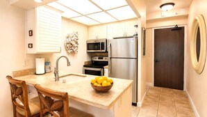 Una cocina con una isla central, sillas de madera, microondas, horno, refrigerador y una puerta con espejo circular.