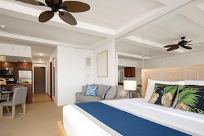 A hotel room with a bed, a desk, a kitchenette, and a ceiling fan. - Whaler | Ocean View Studio Sleeps 2 | Car Incl. w/ 6+ Nights | WH2-465 by KBM (Lahaina)