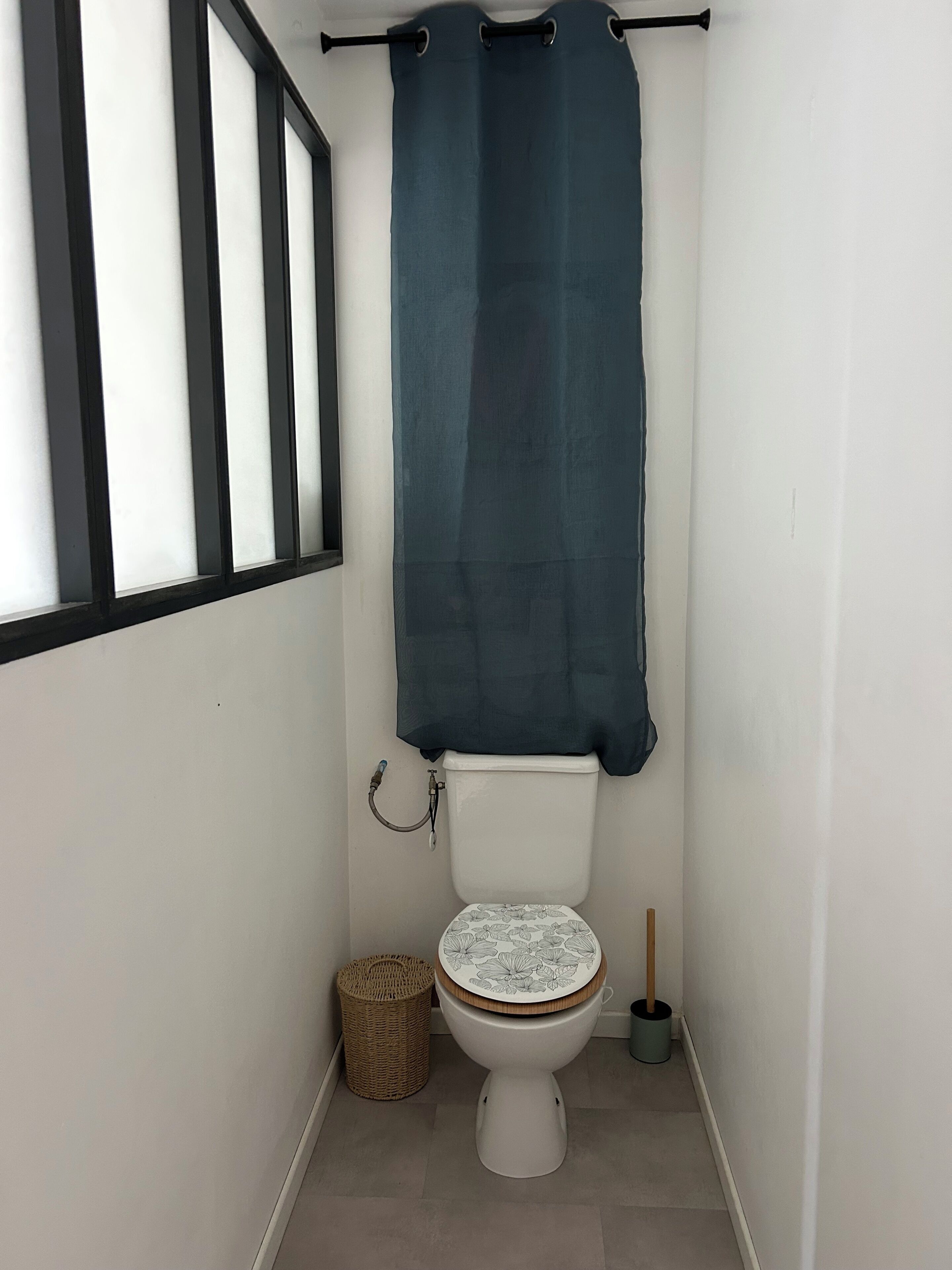 A small, clean bathroom with a toilet, a wicker basket, and a broom.