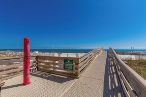 Ein Holzsteg führt zu einem Strand, an dem ein Schild darauf hinweist, dass keine Badeaufsicht gewährleistet ist und Glas nicht erlaubt ist.