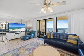 Ein Wohnzimmer mit einem großen Flachbildfernseher, einem Deckenventilator und Blick auf den Strand durch die Schiebetüren.
