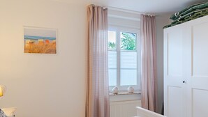 Et soveværelse med seng, et vindue med gardiner, en radiator og en dør.