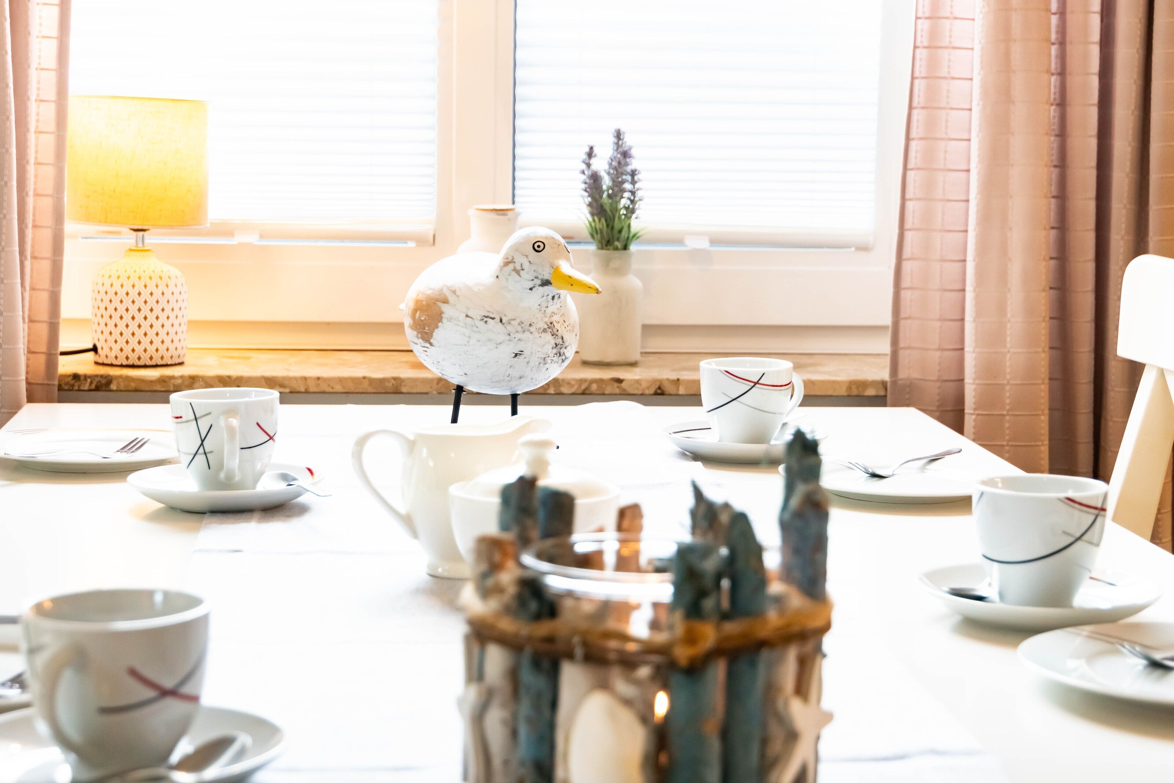 Ein Esstisch mit weißem Geschirr, eine Möwe auf dem Tisch und eine Lampe im Hintergrund.