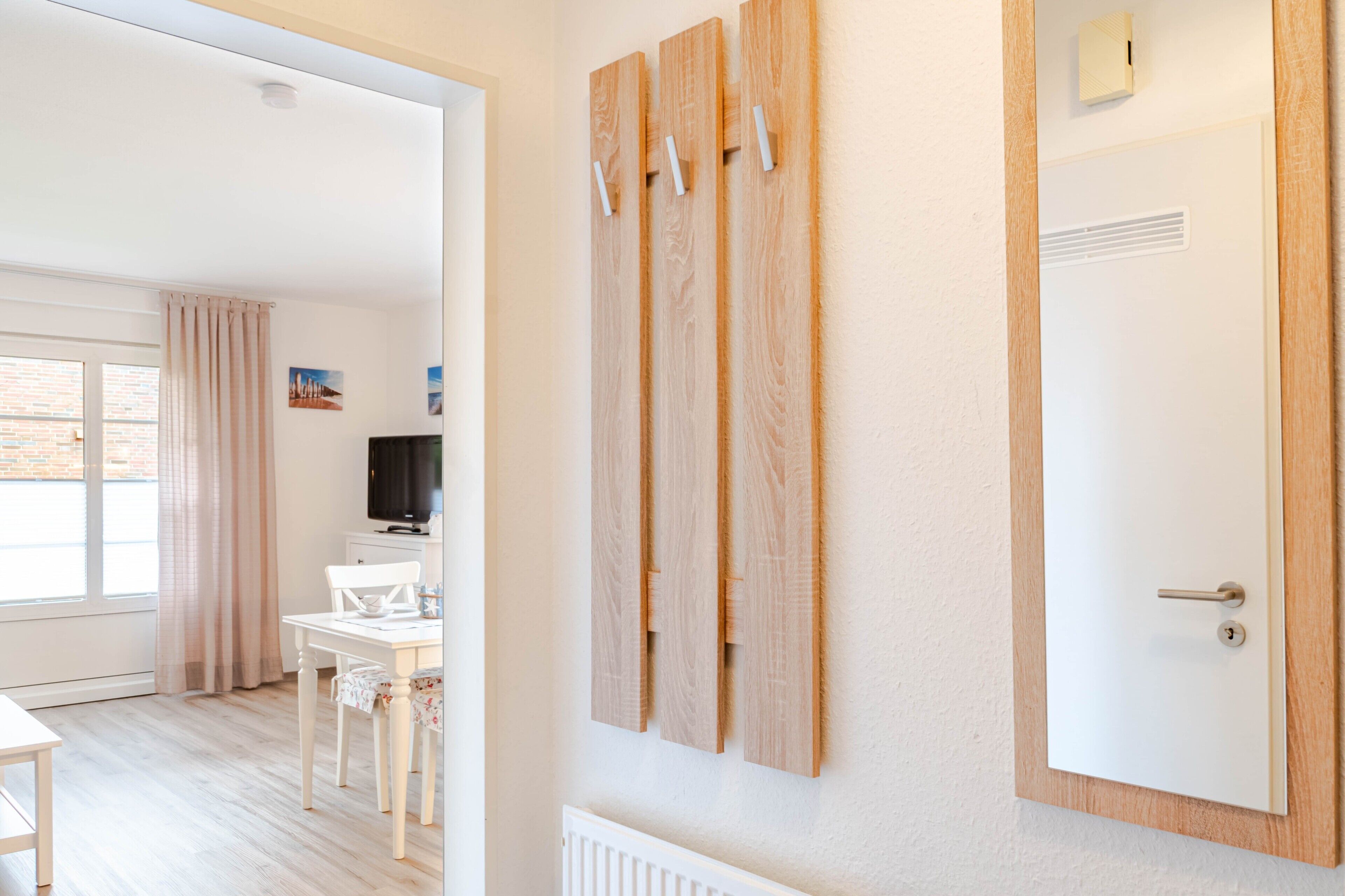 Ein Hotelzimmer mit weißer Tür, einem Heizkörper, einem Fernseher, einem Esstisch mit Stühlen und einem Fenster mit Vorhängen.