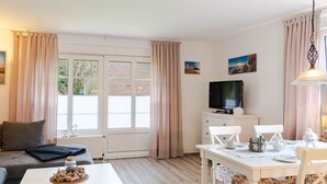 A room with a sofa, a dining table set with chairs, a television, and a window with curtains.