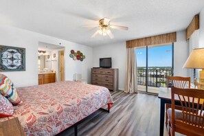 Ein Hotelzimmer mit Bett, Schreibtisch, Stuhl, Fernseher, Deckenventilator und einem Balkon mit Blick.