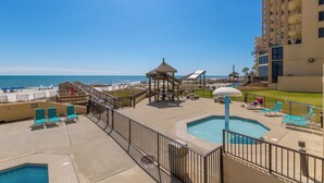 Área de piscina en un resort, con vista a la playa, una estructura de juegos para niños y una piscina pequeña.