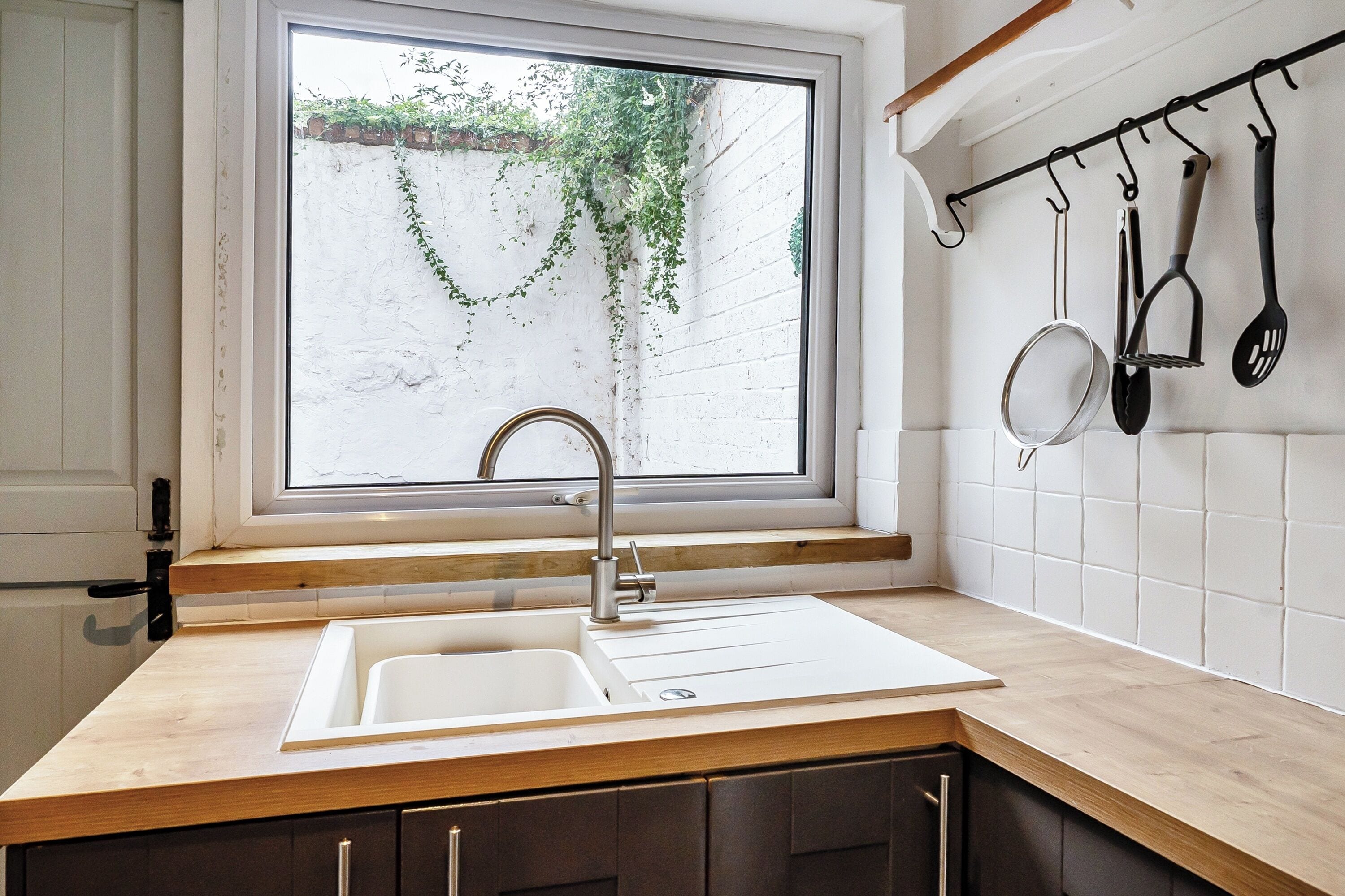 A kitchen with a window, a sink, and a utensil rack.