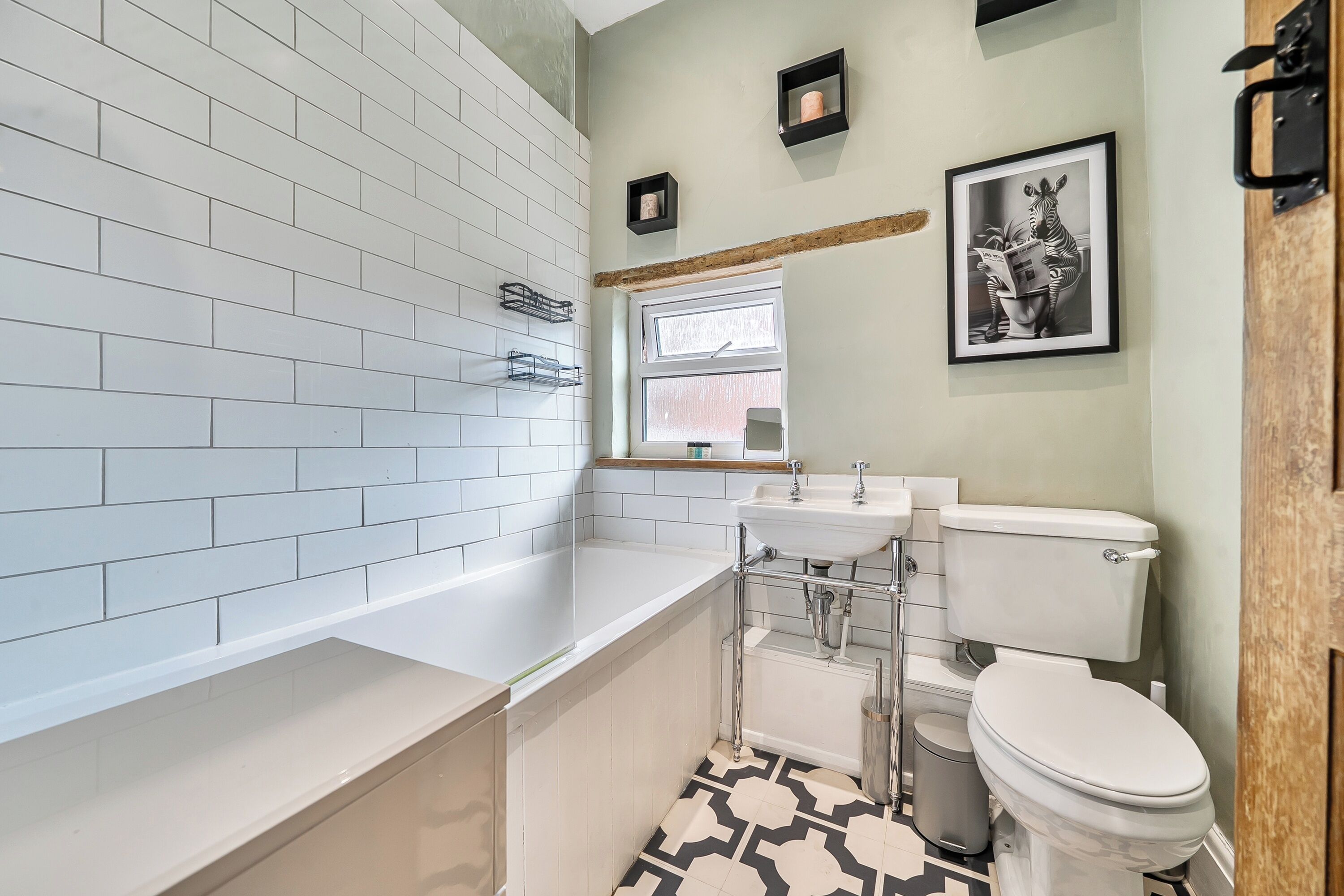 A bathroom with white subway tiles, a white sink, a toilet, and a framed picture on the wall.